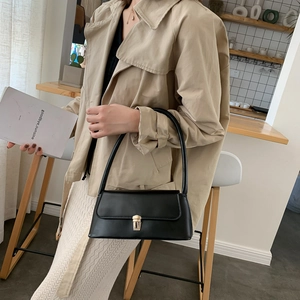 Sac sous le bras élégant en cuir noir avec boucle dorée dans un décor intérieur chaud