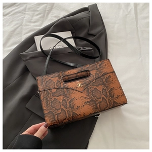 Close-up of brown snakeskin textured envelope bag with gold logo on dark grey blazer