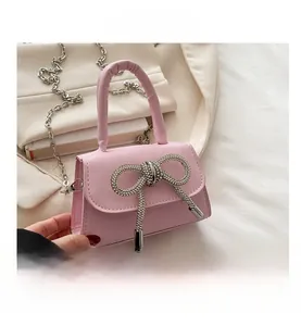 Detail van roze mini-handtas met een glanzende strass-strik en een metalen kettingriem