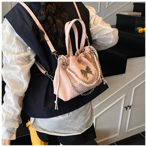Pink drawstring backpack with silver butterfly detail and pearl chain worn by a model