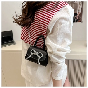 Détail du mini sac en cuir noir avec nœud en strass argenté porté par un mannequin