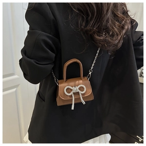 Détail d'un mini sac marron avec un grand nœud en strass et une bandoulière en chaîne