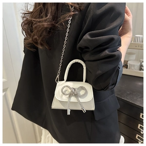 Détail d'un mini sac blanc avec un grand nœud en strass et une bandoulière en chaîne
