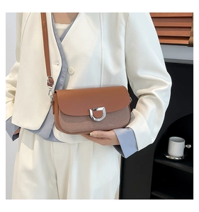 Detail of brown leather flap crossbody bag with silver D-buckle and woven texture