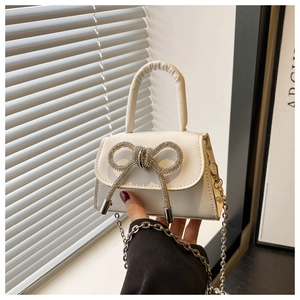 Détail d'un sac à main blanc avec un grand nœud en strass et une bandoulière en chaîne