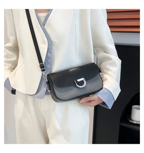 Detail of grey and black crossbody bag with metallic D-ring buckle on white blazer