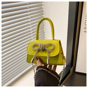 Détail du mini sac vert néon avec nœud en strass et chaîne argentée tenu à la main
