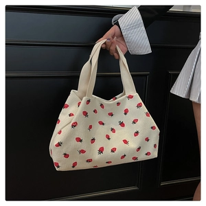 Detail shot of strawberry embroidery on off-white corduroy tote bag with soft texture