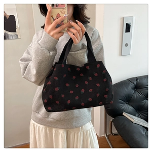 Detail of a black corduroy tote bag with red strawberry print shown on a shoulder