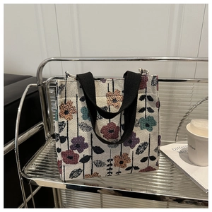 Detail of floral tapestry tote bag with wide black straps on a metal display rack