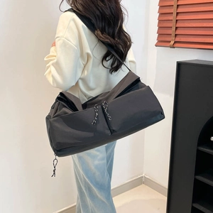 Grand sac de voyage noir à poches multiples porté par un mannequin dans un décor naturel