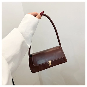 Detail of dark brown leather baguette bag with shiny finish and golden metal buckle