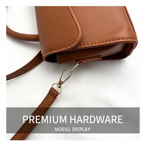 Detailed close-up of light gold metal hook and caramel leather shoulder strap
