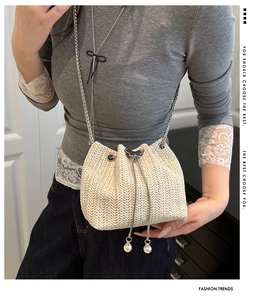 Detail of off-white woven bucket bag featuring drawstring closure and pearl charm accents