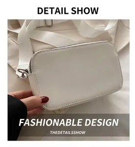 Detail view of white rectangular crossbody camera bag with wide fabric strap and metal hooks