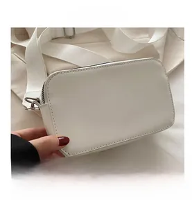 Detail view of white rectangular crossbody camera bag with wide fabric strap and metal hooks