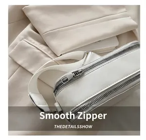 Close-up of dual silver metal zippers on a white textured crossbody camera bag