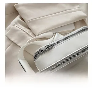 Close-up of dual silver metal zippers on a white textured crossbody camera bag