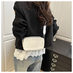 Close-up of minimalist white crossbody camera bag with double zippers and wide fabric strap
