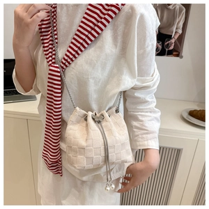 Detail of a beige woven bucket bag with silver chain strap and pearl drawstring charms