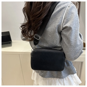Rear view of model wearing a black rectangular crossbody bag with a wide fabric strap