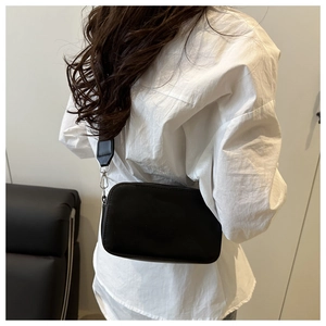 Minimalist black crossbody camera bag with adjustable strap worn on a white shirt