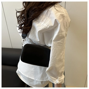 Detail view of black litchi texture crossbody bag with wide strap on a model