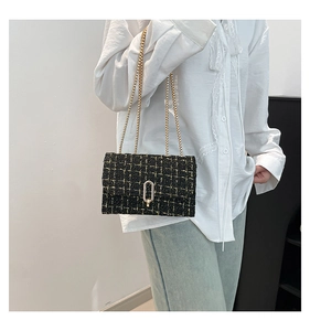 Modèle portant un sac bandoulière en tweed noir et doré avec chaînes métalliques élégantes