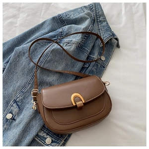 Détail d'un sac besace marron avec boucle fer à cheval dorée sur une veste en jean