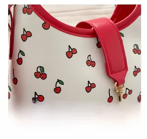 Close-up of red cherry pattern print on white leather bag with golden metal buckle