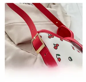 Detail of white bag with cherry print featuring adjustable strap and gold metal buckle