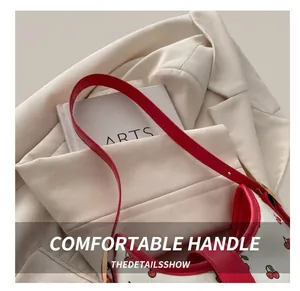 Close-up of white leather handbag with red cherry print and red handle with gold hardware