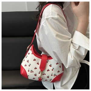 Close-up of a white shoulder bag with red cherry prints and red leather trim detail