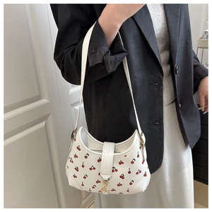 Close-up of a white hobo bag featuring red cherry patterns and a gold metal buckle detail