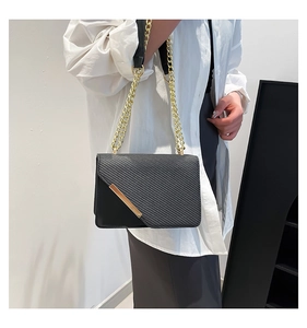 Detail of black textured crossbody bag with gold chain strap and metal trim on model