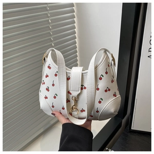 Close-up of white shoulder bag featuring vibrant red cherry prints and gold metal clasp
