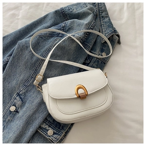 Détail du sac selle blanc avec fermoir en U doré sur fond de veste en jean bleue