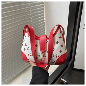 Detail of red cherry print on white leather handbag with golden metal hardware
