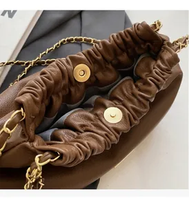 Detail of dark brown bucket bag featuring gold magnetic clasp and woven chain strap