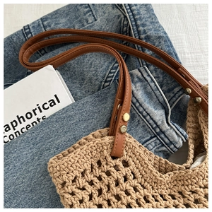 Close-up of beige woven beach bag with leather handles and metallic rivet details