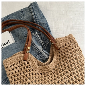 Detail of woven straw tote bag featuring brown leather handles and gold rivet accents