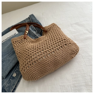 Detail of hand-woven beige tote with dark brown leather handles and gold metal rivets