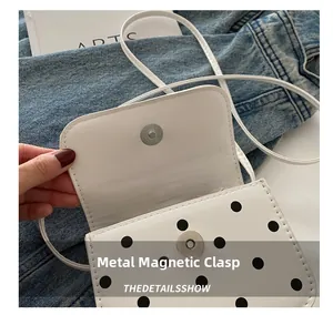 Detail shot of the magnetic metal clasp on a white polka dot mini crossbody bag
