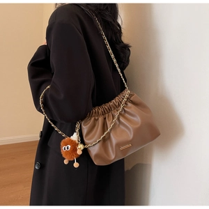 Detail of a brown pleated bucket bag with gold chain strap and plush pendant on coat