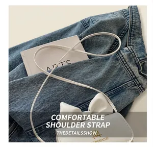 Detail of white mini crossbody bag with bow decoration and gold logo on denim jacket