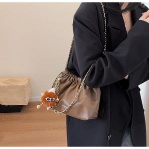 Detail of dark brown pleated bucket bag with gold chain strap and fuzzy eye charm