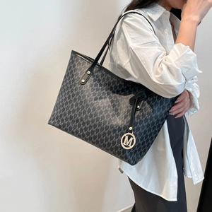 Détail d'un grand sac cabas noir avec motif M et breloque logo en métal doré