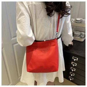 Détail du sac seau en cuir mat rouge avec fermoirs métalliques et bandoulière fine