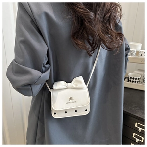 Close-up of a white mini crossbody bag with a bow and brand logo worn by a model
