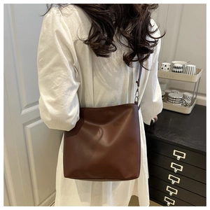 Détail du sac seau en cuir marron foncé montrant sa texture mate et ses boucles métalliques